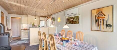 Un comedor con mantel a rayas, sillas de madera y una cocina al fondo.