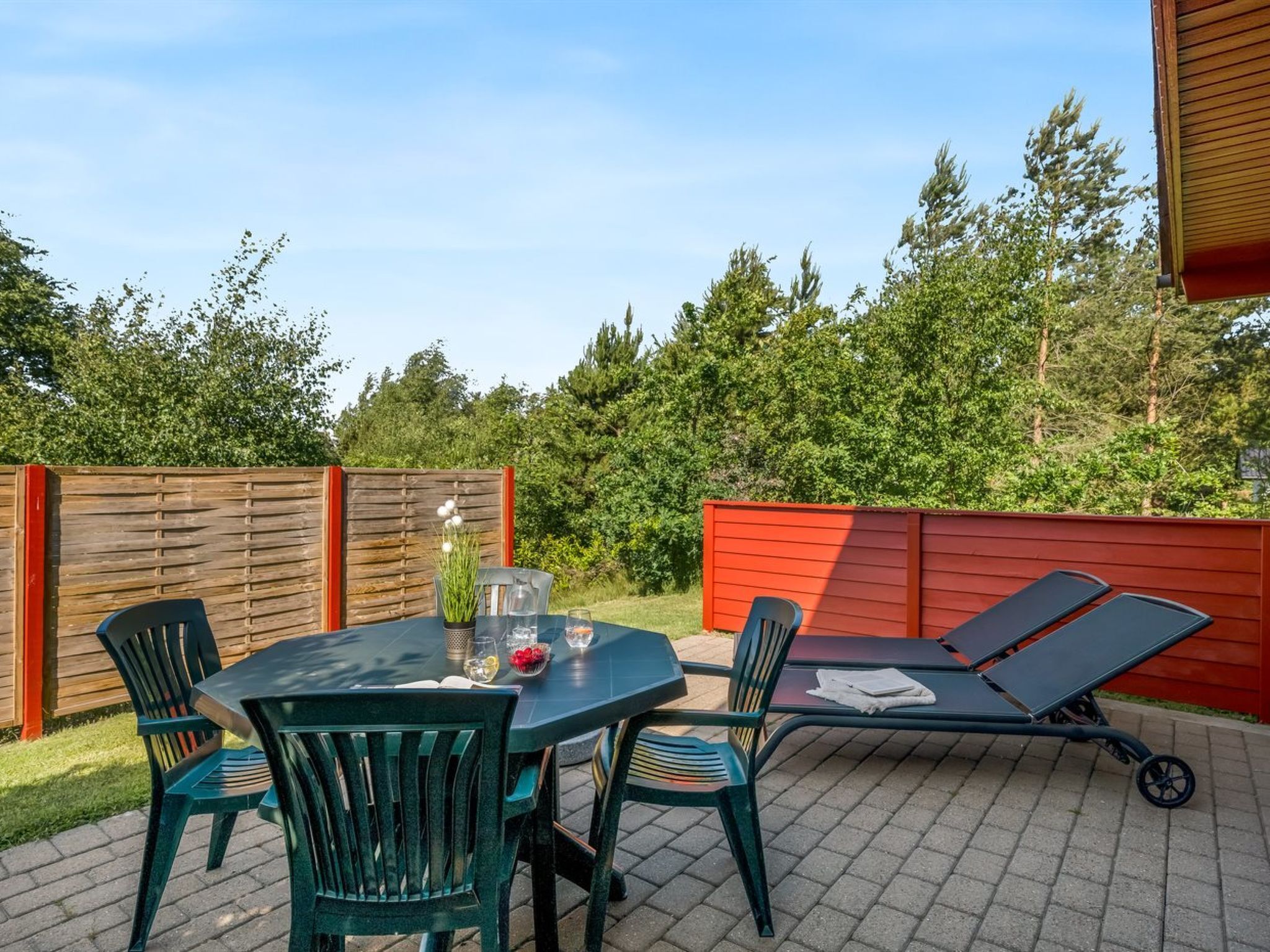 An outdoor patio with a table, chairs, and a sun lounger.