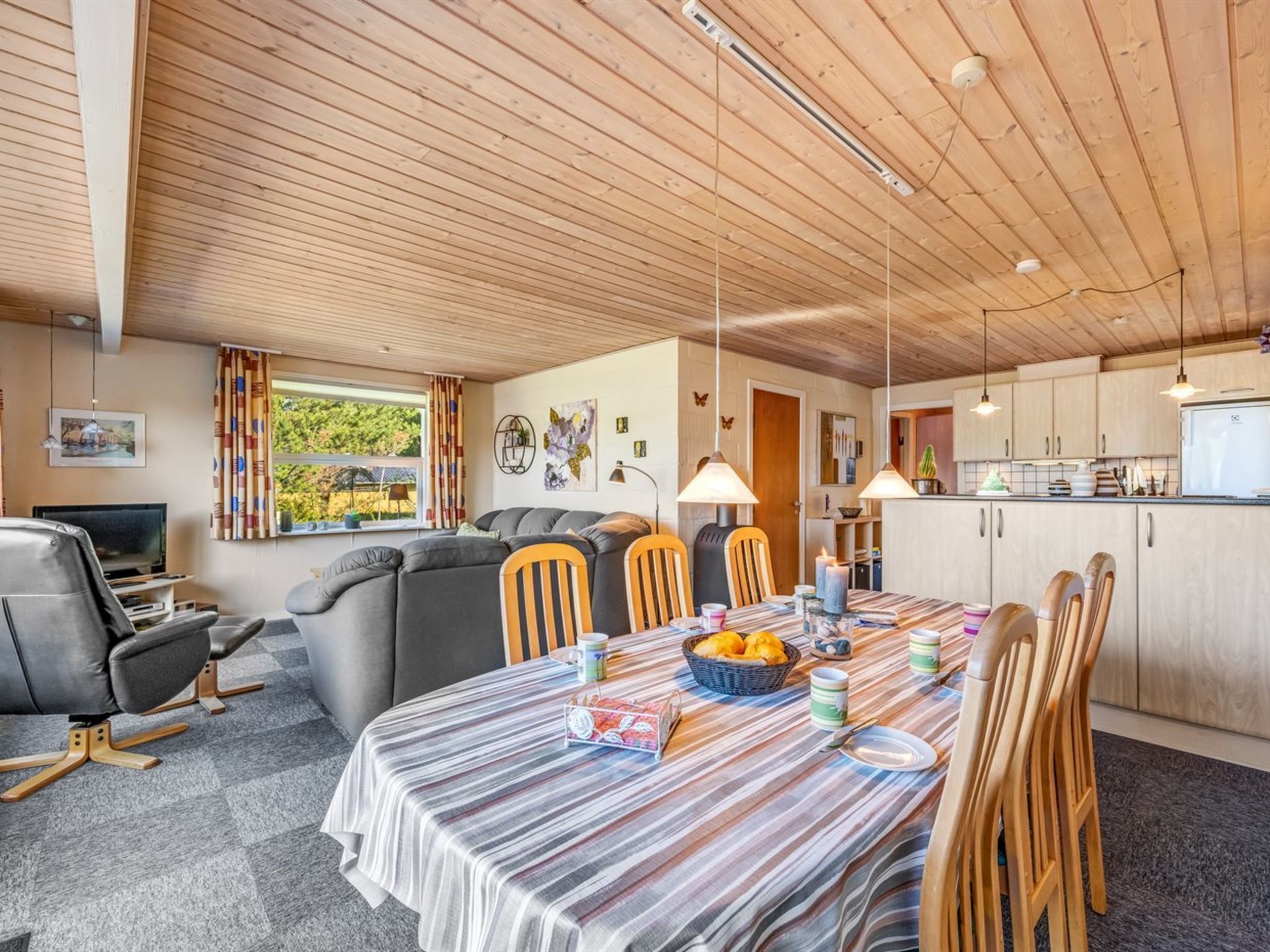 Un salon confortable avec un canapé, une table à manger et des chaises, un coin cuisine avec des placards et un réfrigérateur, et une fenêtre avec des rideaux.
