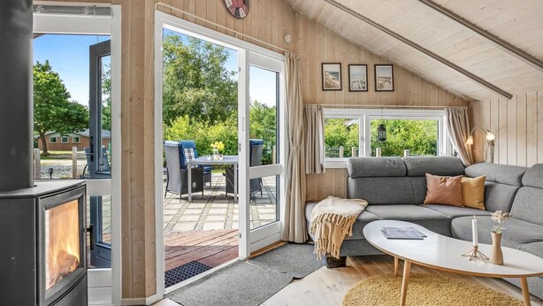 Ein gemütliches Zimmer mit Kamin, einer Couch, einem Esstisch und Blick ins Freie.