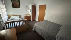 Quarto com cama de madeira, mesa de cabeceira, cômoda pequena, espelho e porta que dá para outro cômodo.