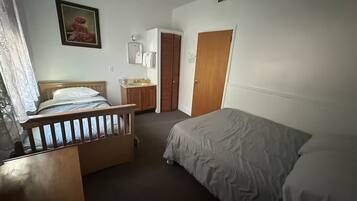 A bedroom with a wooden bed, a bedside table, a small dresser, a mirror, and a door leading to another room.