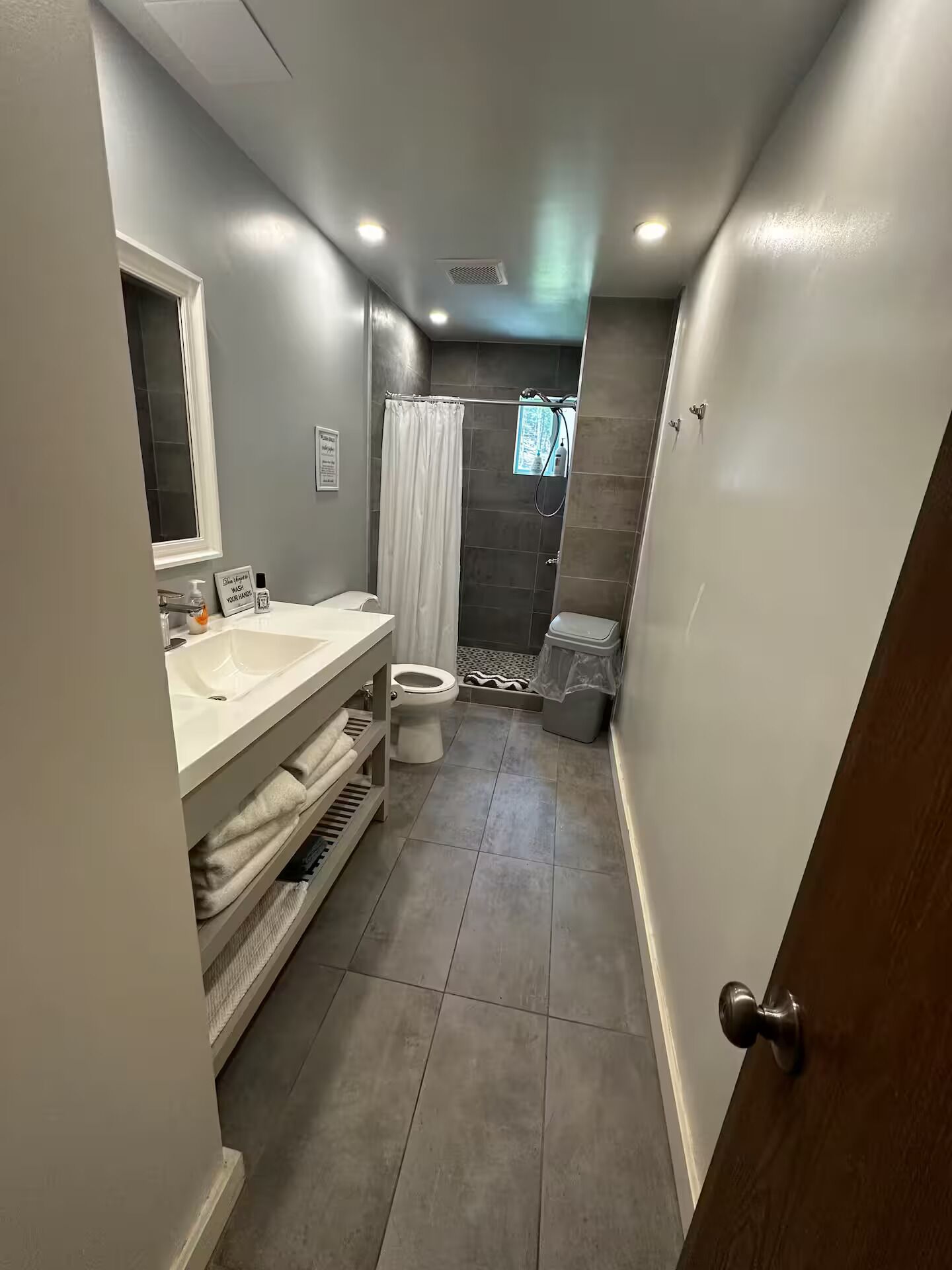 A narrow bathroom with a toilet, sink, and shower area.
