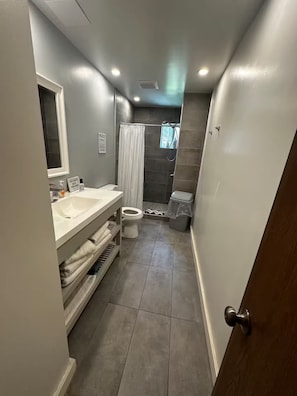 A narrow bathroom with a toilet, sink, and shower area.