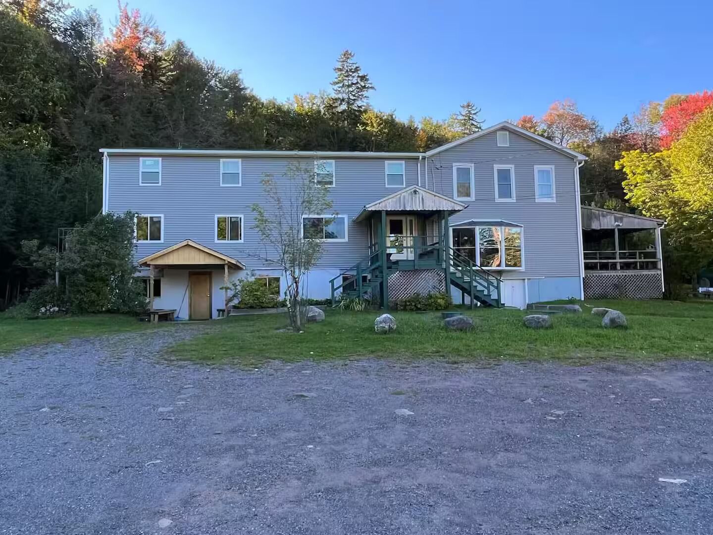 A two-story building with a porch, a covered staircase, and a small front yard with rocks and a tree.