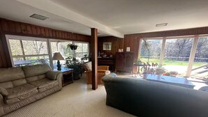 Uma sala de estar ampla com uma grande janela, um sofá, uma mesa de centro e um piano.