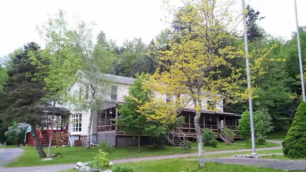 Uma casa de dois andares com varanda frontal, escadaria visível e gramado bem cuidado.