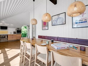 Eine moderne Küche mit weißen Schränken, einem Holztisch, Korbstühlen und Pendelleuchten.