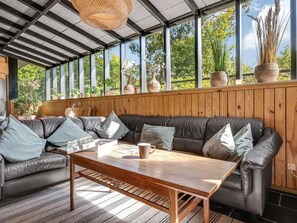 Ein modernes Wohnzimmer mit Ledersofa, Holztisch und großen Fenstern mit Blick auf Grünflächen.