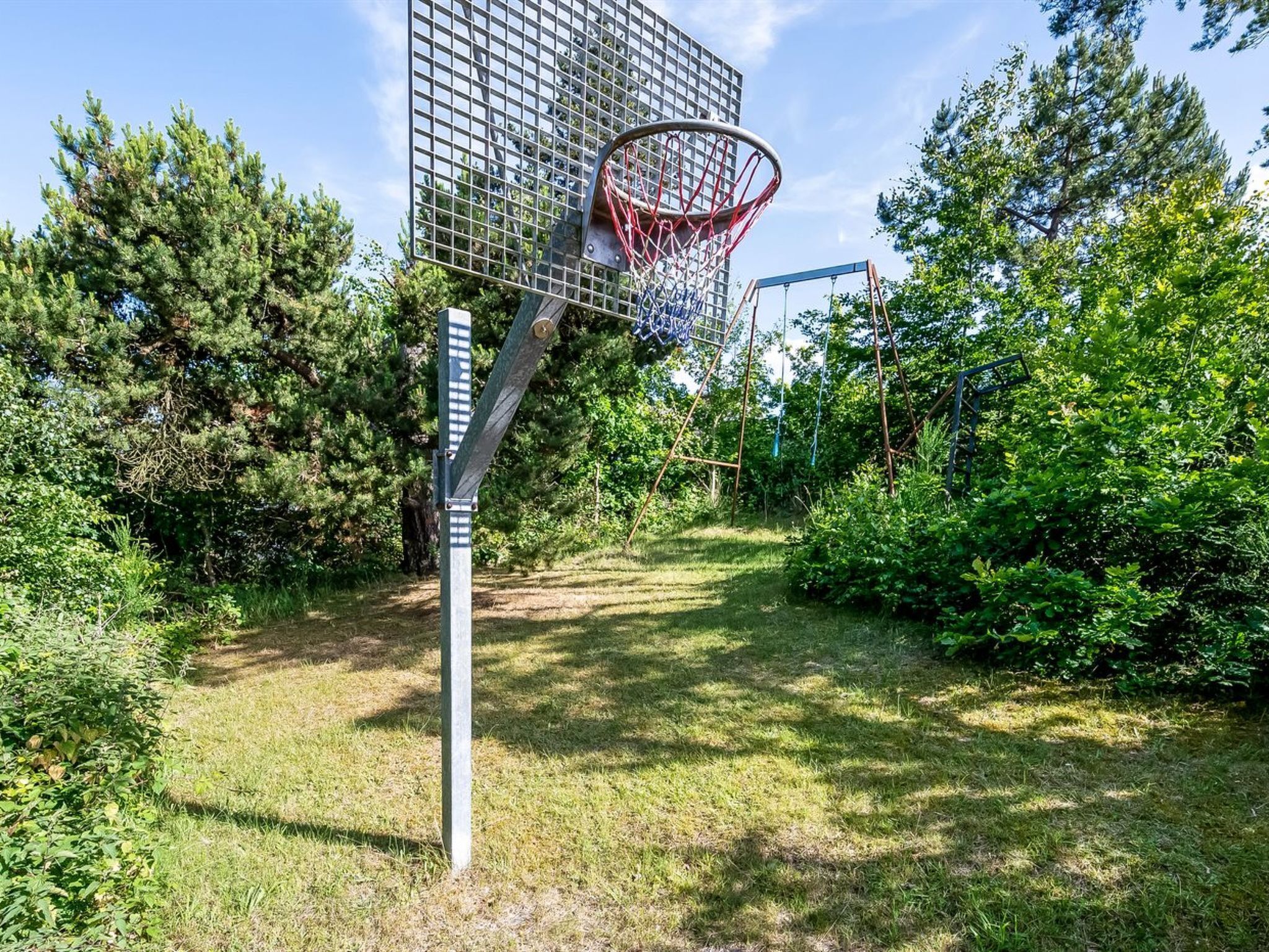 A basketball hoop in a grassy area with trees and a building in the background.