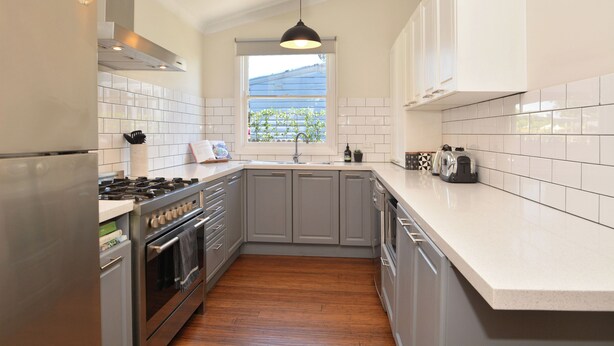 A kitchen with grey cabinets, a stainless steel refrigerator, a stove, and a window with a view of greenery. - Linda’s Cottage at the Hunter  (Cessnock)
