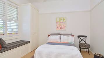 A bedroom with a bed, a bench, a chair, a wall sign, and a window with blinds.