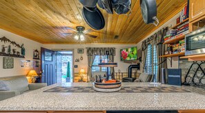 Een blokhutinterieur met houten plafond, open haard, televisie en een keukenhoek.