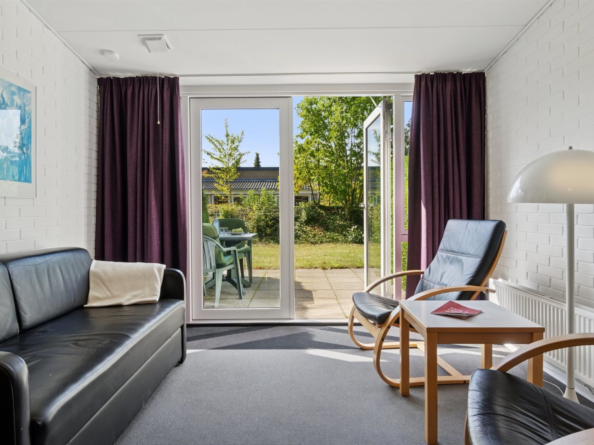 A modern room with a sofa, two chairs, a table, and a lamp.