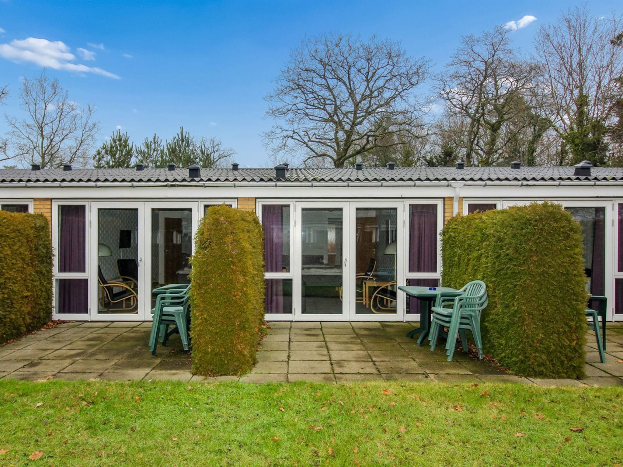 A row of single-story buildings with sliding glass doors, outdoor seating, and a well-maintained lawn.
