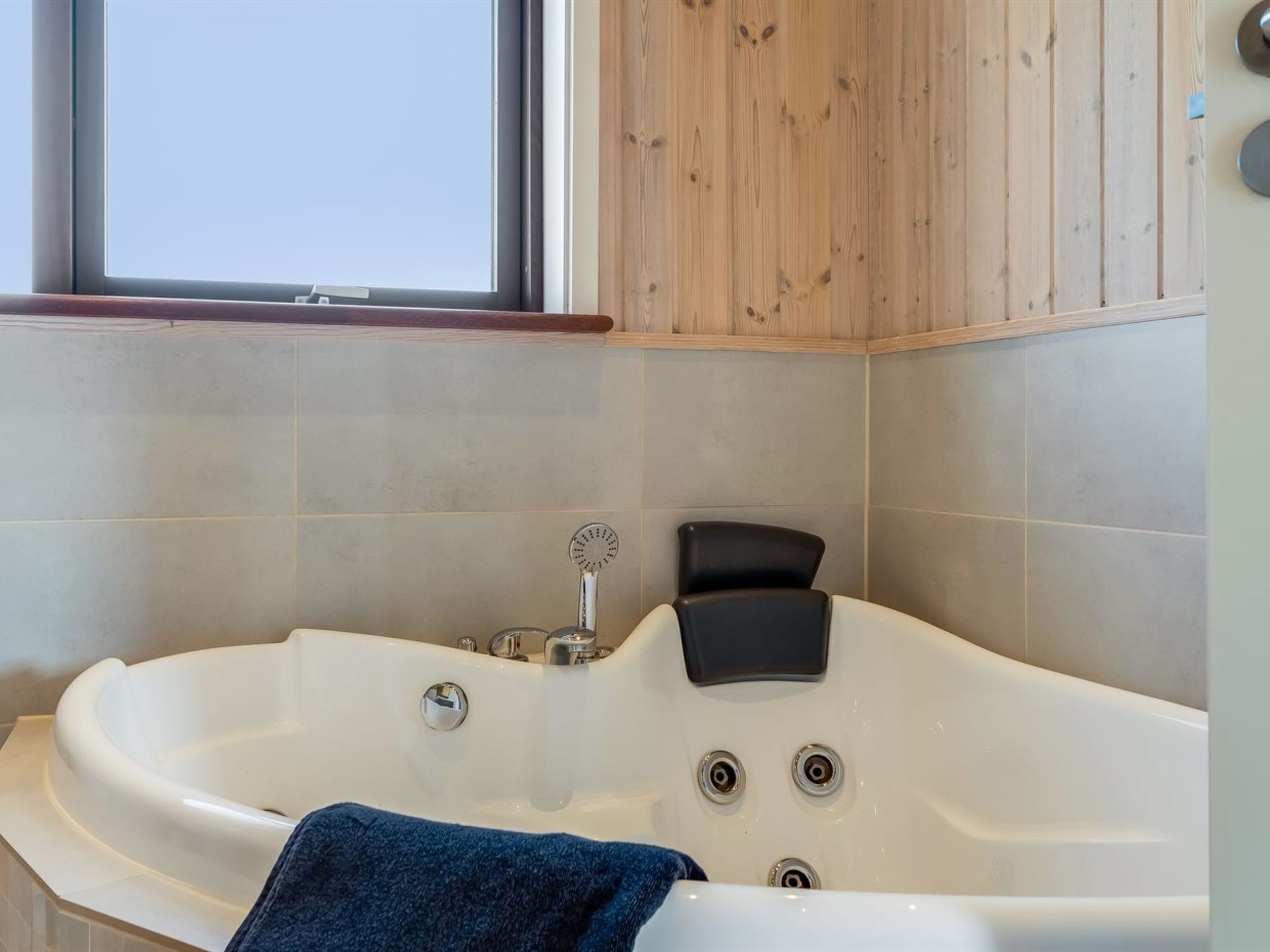 A modern bathroom with a freestanding bathtub, a window, and wooden paneling.