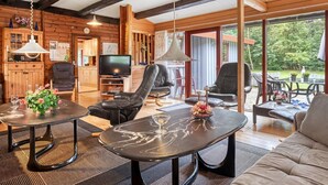 Interior acogedor de una cabaña con detalles de madera, un televisor, sillones de cuero y una mesa de comedor.