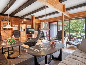Ein gemütliches Blockhaus-Interieur mit Holzvertäfelung, einem Fernseher, Ledersesseln und einem Esstisch.