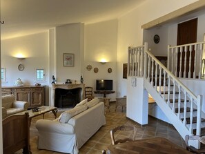 A living room with a fireplace, sofa, TV, and a staircase. - Villa Manou with private pool (LORGUES)