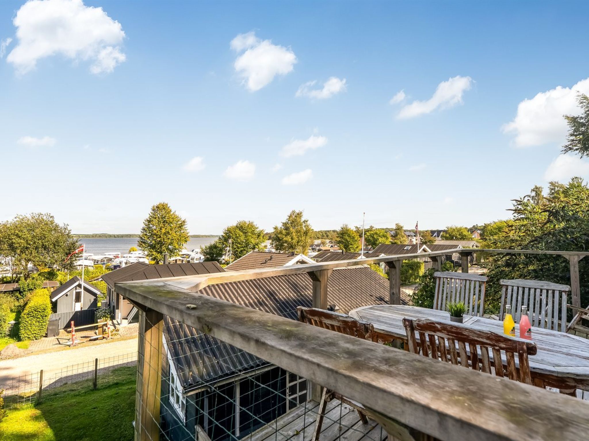 A rooftop terrace with a view of a lake, a wooden deck, and a table with chairs.