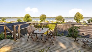 Een terras met een tafel en stoelen, zonnepanelen, en uitzicht op een meer en boten.