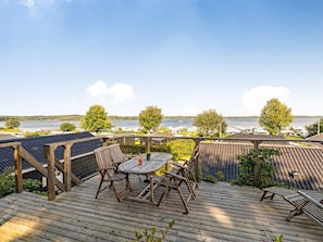Une terrasse avec une table et des chaises, des panneaux solaires et une vue sur un lac et des bateaux.