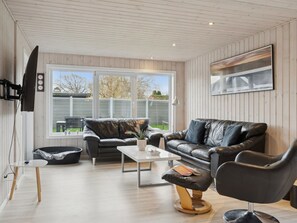 Ein modernes Wohnzimmer mit einer Ledersofa, einem Couchtisch, einem schwarzen Sessel und einem an der Wand befestigten Fernseher.