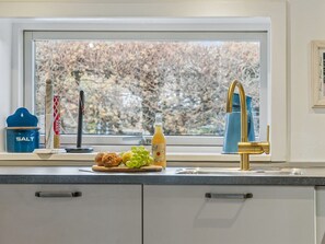 Eine Küche mit Fenster, Spüle, einem blauen Salzbehälter, einer Orangensaftflasche und einem Teller mit Brot und Trauben.