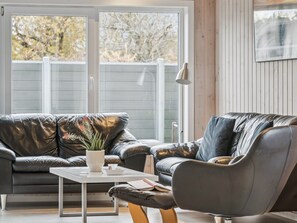 Ein modernes Wohnzimmer mit Ledersofas, einem weißen Couchtisch und einem großen Fenster mit Blick auf Bäume.