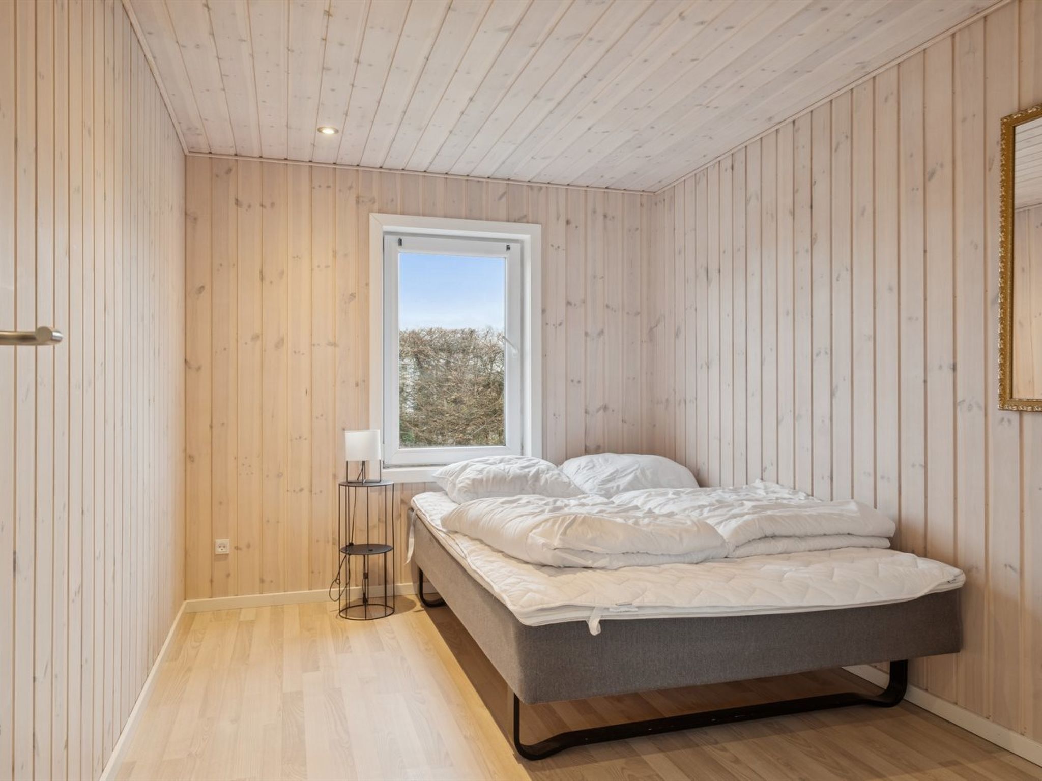 Quarto com cama, janela e paredes de madeira.