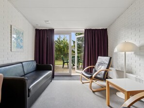 Ein modernes Zimmer mit einem schwarzen Ledersofa, einem hölzernen Schaukelstuhl, einem weißen Tisch und einer Stehlampe.