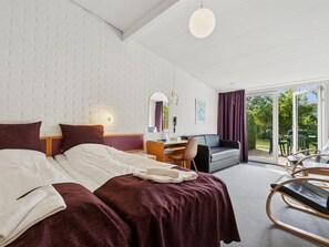 Ein Hotelzimmer mit Bett, Schreibtisch, Stuhl, Sofa und Blick ins Freie.