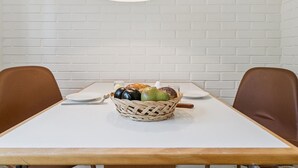 Una mesa de comedor con una cesta de mimbre para frutas, dos sillas marrones y un mantel blanco.
