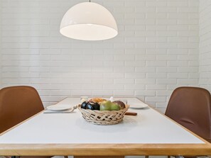 Ein Esstisch mit einem Korbfruchtregal, zwei braunen Stühlen und einer weißen Tischdecke.
