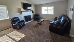 A living room with a fireplace, a television mounted above it, a sofa, a chair, and a coffee table. - Cozy house in the heart of Willow Springs (Rosamond)