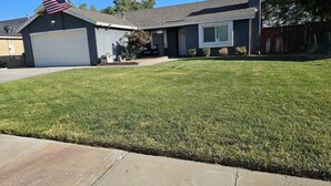 A residential house with a garage, a well-maintained lawn, and a flag on the roof. - Cozy house in the heart of Willow Springs (Rosamond)