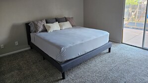 A bedroom with a bed, a carpeted floor, and a sliding glass door to the outside. - Cozy house in the heart of Willow Springs (Rosamond)