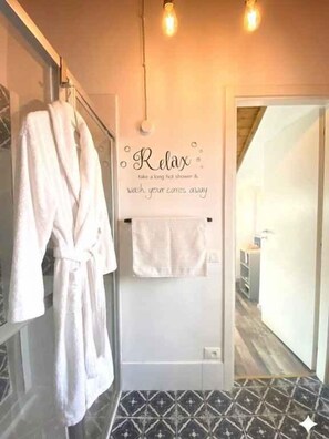 Ein Badezimmer mit Handtuchhalter, Bademantel und einem Schild an der Wand mit der Aufschrift 'Entspannen Sie sich, nehmen Sie eine lange heiße Dusche und lassen Sie den Alltagsstress hinter sich.'