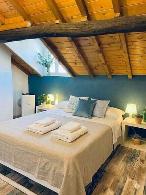Ein Schlafzimmer mit Holzboden, einem Bett mit weißen Leinen, einem Nachttisch mit Lampe und einem Fenster mit Pflanze.