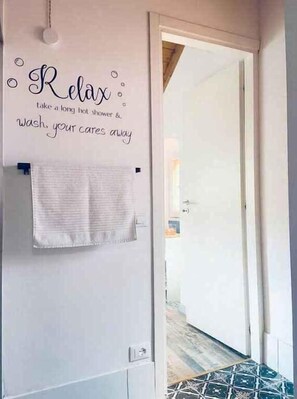 Ein Badezimmer mit einem Handtuch an einem Halter, einem Schild mit dem Wort 'Relax' und einer Information zum Genießen einer langen heißen Dusche.