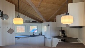 Una cucina con travi in legno al soffitto, lampade a sospensione, lavastoviglie e frigorifero.