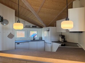 Eine Küche mit Holzbalkendecke, Pendelleuchten, einem Geschirrspüler und einem Kühlschrank.