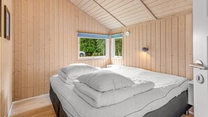 Una stanza con pareti in legno e soffitto spiovente, un letto con biancheria bianca, una finestra che si affaccia sul verde e un lampadario fissato al muro.