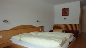 Habitación de hotel con cama de madera, mesita de noche, una pequeña mesa, sofá rojo e iluminación empotrada en la pared.