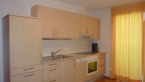Cocina compacta con lavaplatos, estufa y lavavajillas, armarios de madera y una ventana con cortinas.