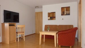 Een woonkamer met een televisie, houten meubels, een bank en twee kunstwerken aan de muur.