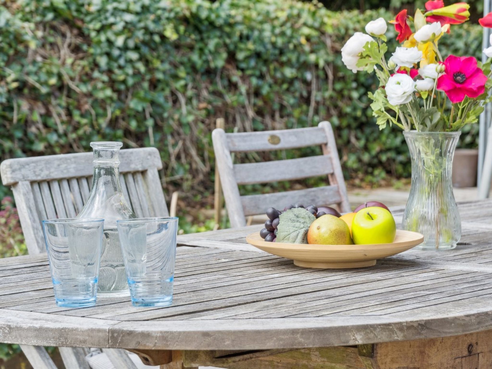 Ein Holztisch mit einer Fruchtschale, einer Blumenvase und zwei Glasflaschen.