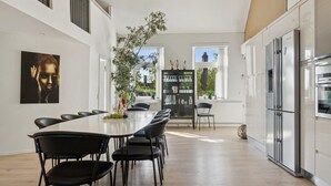 A modern kitchen with a dining area, featuring a long table, chairs, a refrigerator, and a view of the outside. - "Ofelia" - 4km from the sea by Interhome (Nexø)
