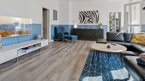 A modern living room with a flat-screen TV, a blue armchair, a black sofa, a round coffee table, and a zebra-patterned wall art piece. - "Ofelia" - 4km from the sea by Interhome (Nexø)