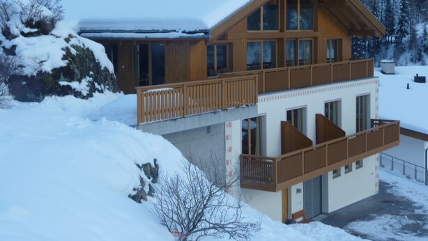 Eine zweistöckige Holzhütte mit Balkonen, umgeben von schneebedeckten Bäumen.
